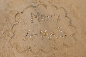 Die Worte "Merry X-Mas" mit Muscheln auf Sand gelegt.