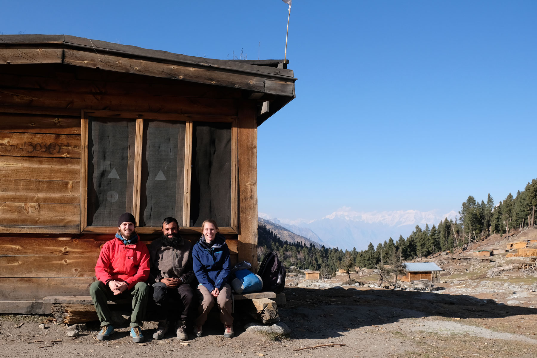 Sebastian und Leo sitzen mit einem pakistansichen Mann vor einer Holzhütte.