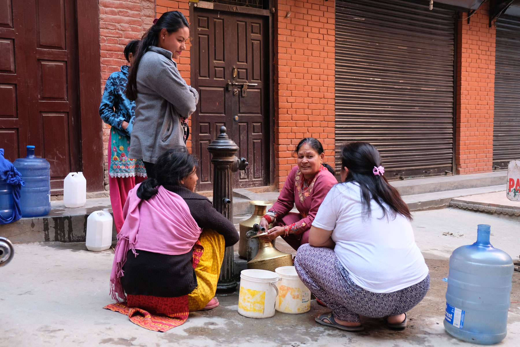 Nepalesische Frauen füllen in Kathmandu Wasser aus einem Brunnen in Kanister.