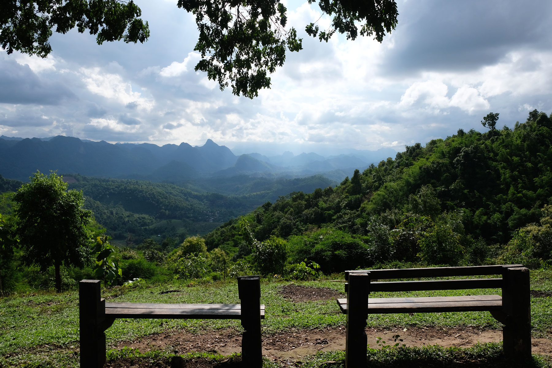 Zwei Sitzbänke stehen oberhalb von bewaldeten Bergen in einem Nationalpark in Thailand.